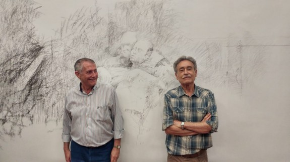 Miguel Massotti y Pedro Cano posan delante del mural que el pintor va a realizar mientras dure su exposición