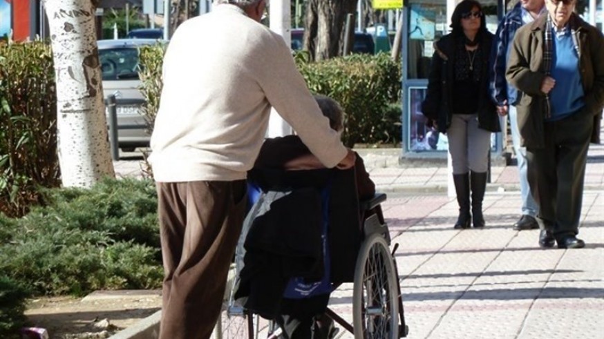 Persona dependiente ayudada por un familiar que empuja su silla de ruedas. EP