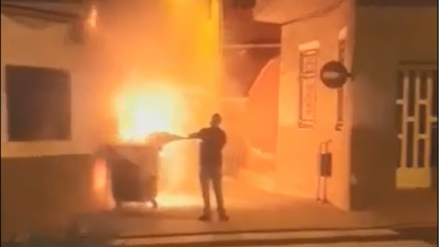 Un vecino intenta apagar el fuego en uno de los contenedores incendiados en Mula