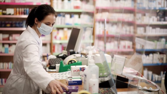 Una farmacéutica con mascarilla despacha en una farmacia