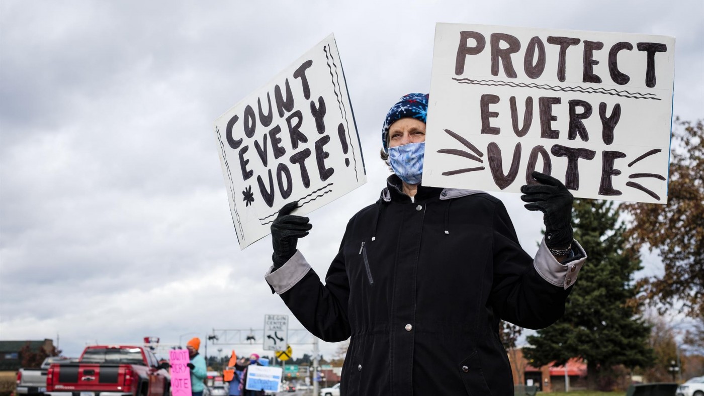 Un activista con dos pancartas en las que se lee "protege cada voto" y "cuenta cada voto! 